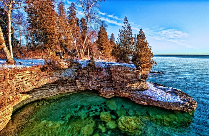 Rocky cliff overlooking clear turquoise water and a forest