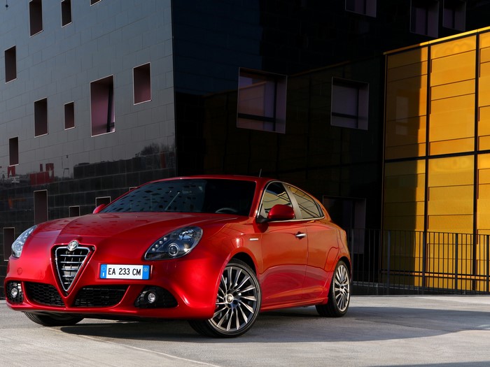 Red Alfa Romeo Giulietta parked in front of modern buildings
