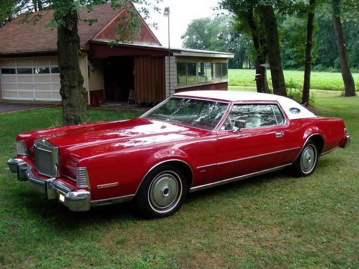 Red Lincoln Mark IV parked on grass near a garage