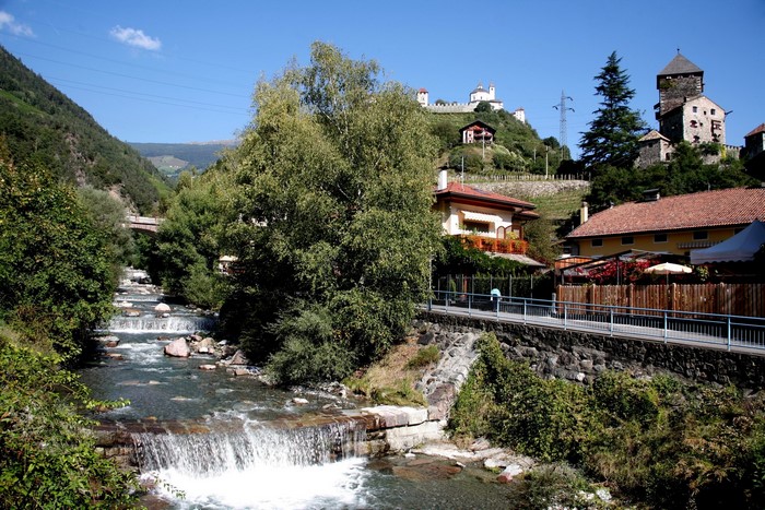 River flowing through a village with castles on a hill in Italy