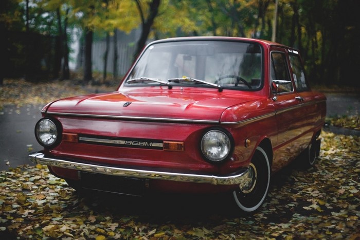 Red retro car parked on a leaf-covered road