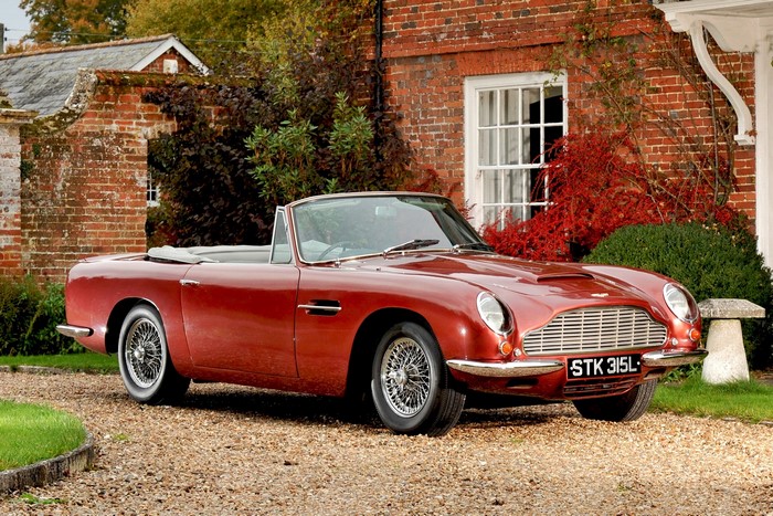 Red Aston Martin DB5 Convertible parked outside brick house