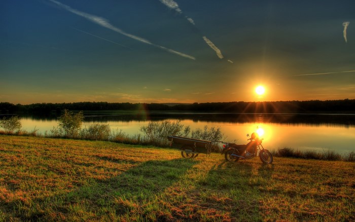 Motorcycle with trailer by a lake at sunset