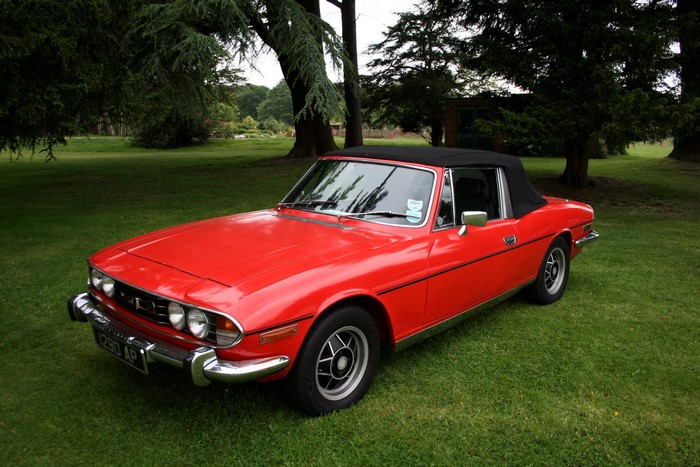 Red Triumph Stag convertible parked on grass