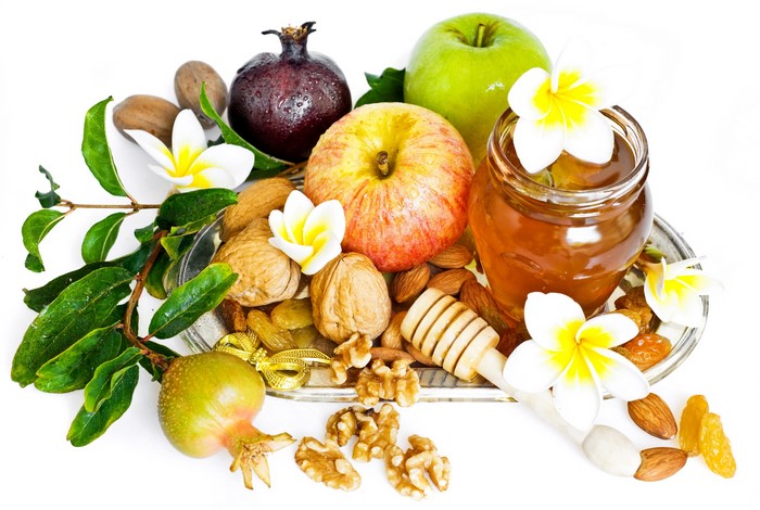 Apples, pomegranates, nuts, raisins, honey, and flowers on a tray