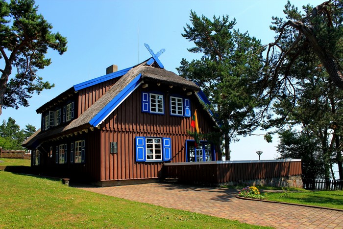 Wooden house with thatched roof and blue shutters in the Baltics