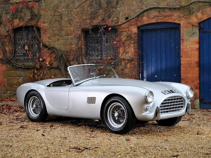 Silver AC Cobra convertible parked outside brick building