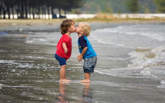 Two young children kissing on a beach