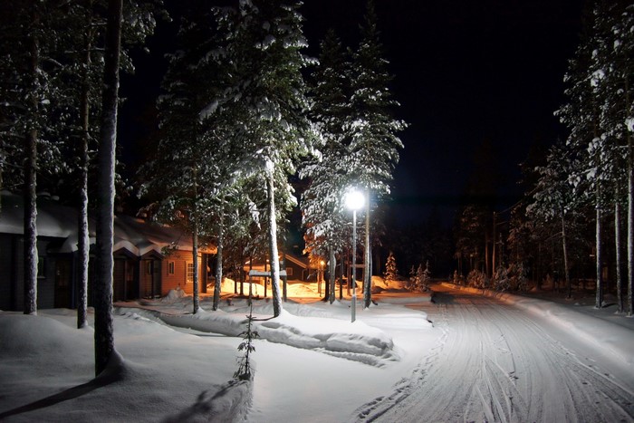 Snowy road at night with houses and trees in Finland