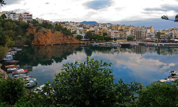 Boats docked in a harbor with buildings and a rocky cliff in Greece