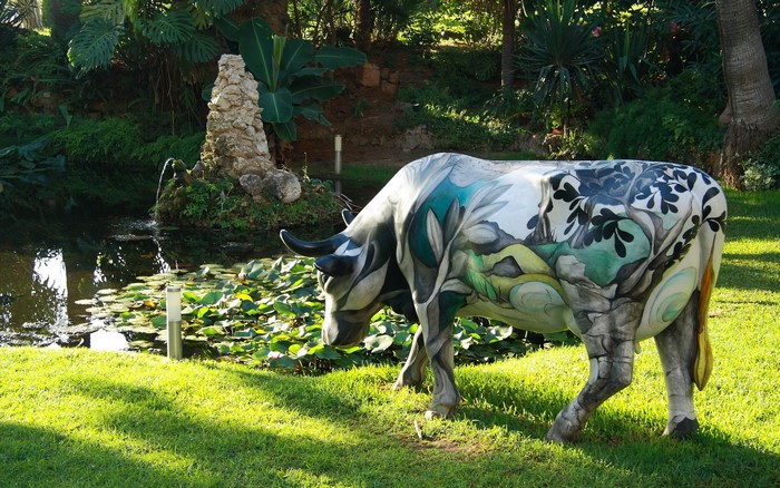 Painted cow sculpture in a park with a pond