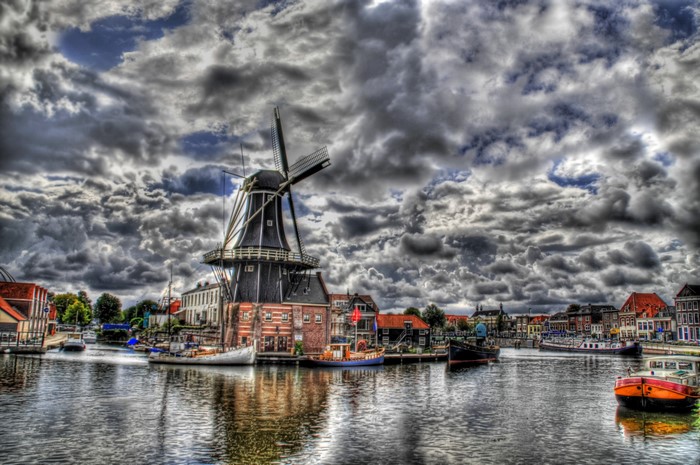 Windmill and boats in a canal under cloudy sky