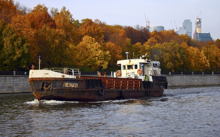 Barge on a river with autumn trees and city skyline