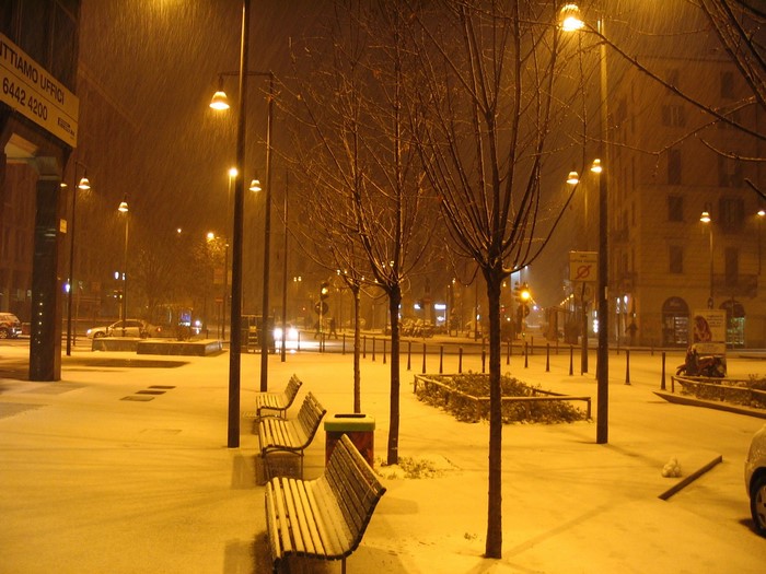 Snowy night in an Italian city with street lights and benches