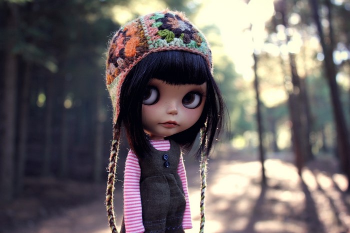 Doll wearing a knitted hat and overalls in a forest