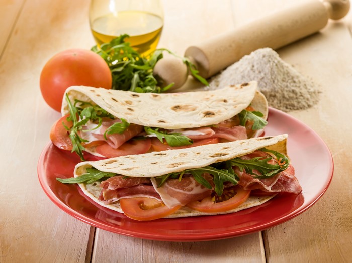 Two piadinas with prosciutto, tomatoes, and arugula on a plate