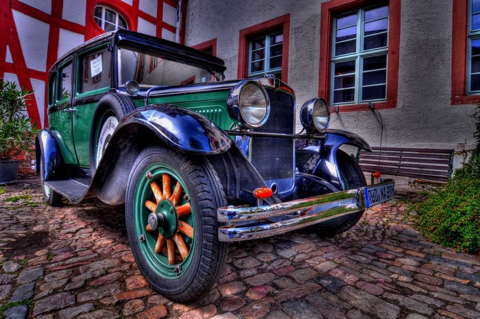 Green vintage car parked on cobblestone street