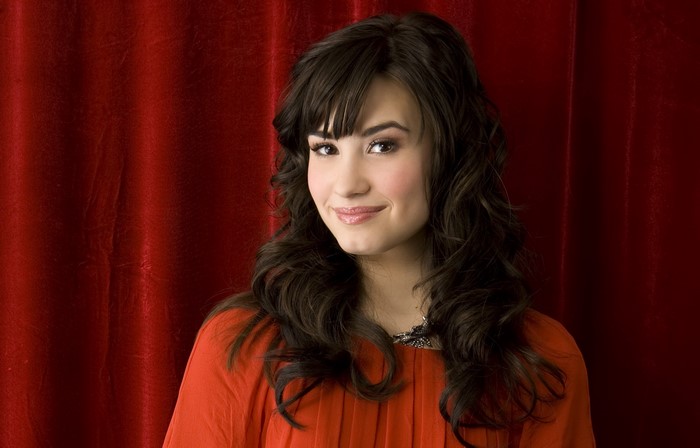 Demi Lovato smiling in front of a red curtain