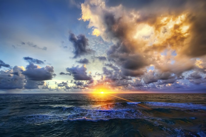 Sunset over the ocean with dramatic clouds and waves