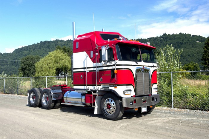 Red and white Kenworth semi-truck parked on a dirt road