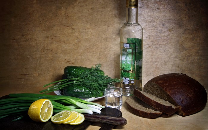 Still life with vodka, bread, cucumbers, lemons, and green onions