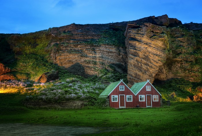 Two red houses with green roofs at the base of a rocky mountain in Iceland