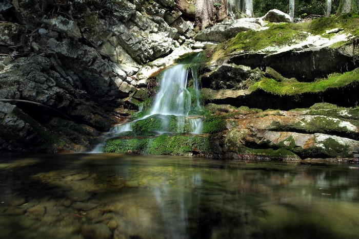 Waterfall cascading over moss-covered rocks into a clear stream