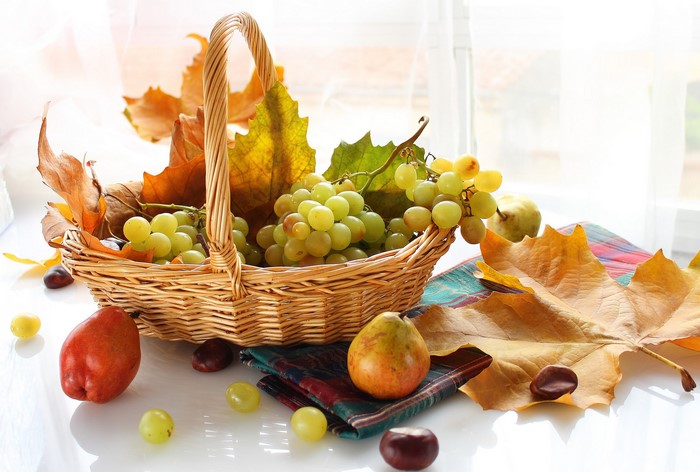 Still life with grapes in a wicker basket and autumn leaves