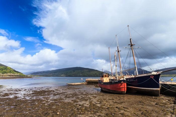 Ships docked on a muddy shore with mountains in the background