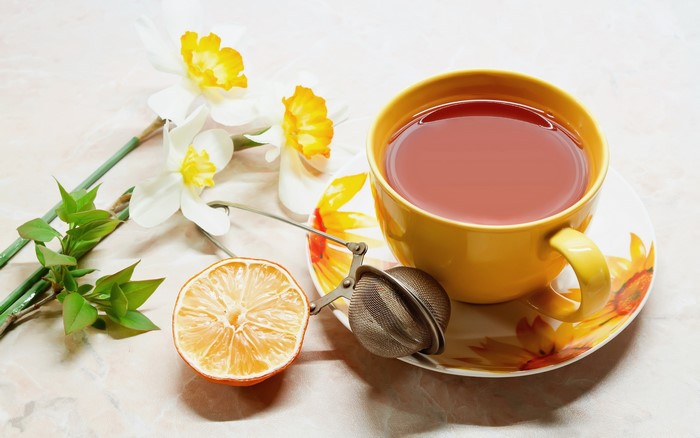 Yellow teacup with tea, daffodils, dried lemon, and tea strainer