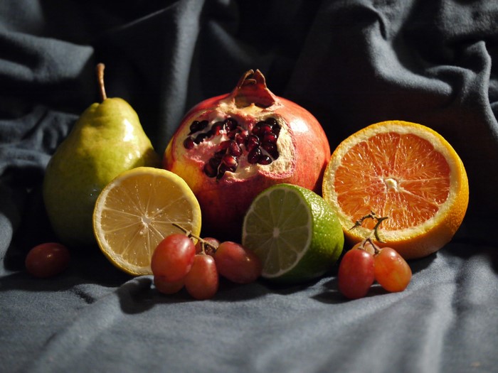 Still life of fruits including pomegranate, orange, lemon, pear, lime, and grapes