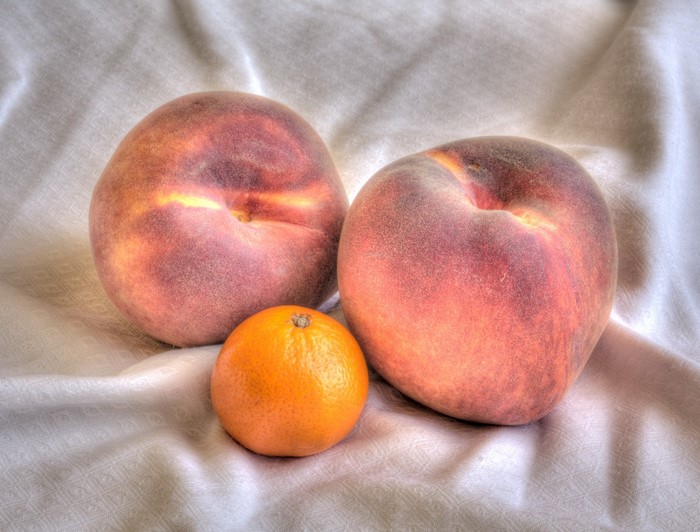 Two peaches and an orange on a white cloth