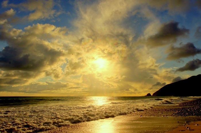 Sunset over the ocean with clouds and a rocky coast