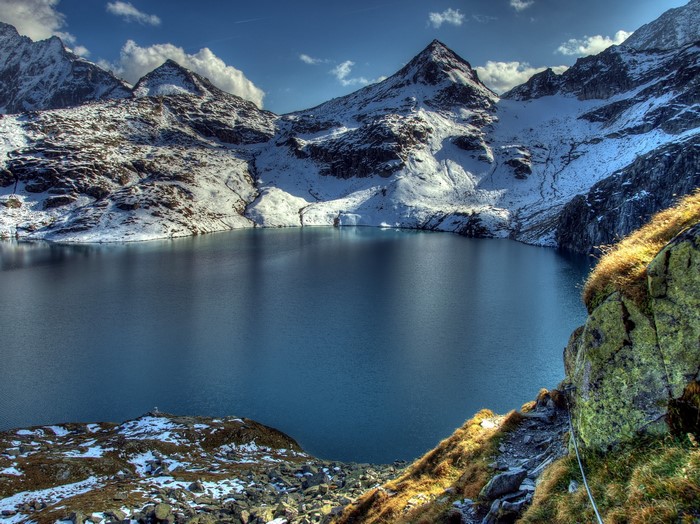 Snow-capped mountains surround a deep blue lake in the Alps