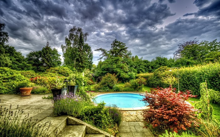 Backyard with a swimming pool and lush garden under cloudy sky