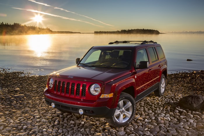 Red Jeep Patriot on a rocky coast at sunrise