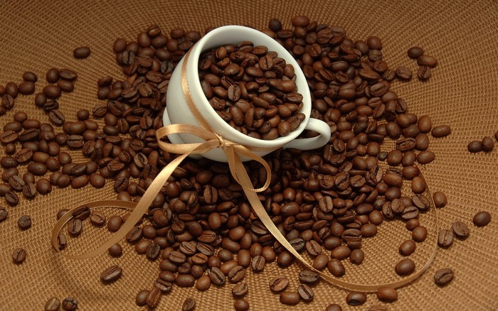Coffee beans spilling from a cup with a ribbon