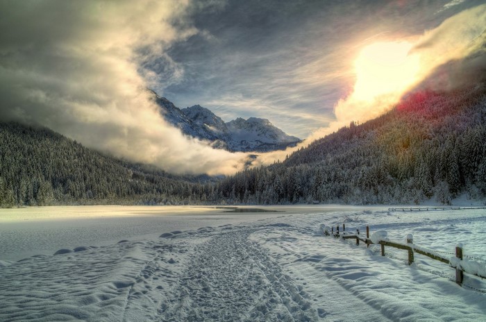 Snowy mountain landscape with sunlit clouds and forest