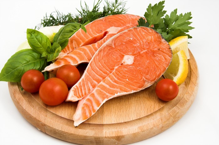 Salmon steaks with tomatoes and herbs on a wooden board