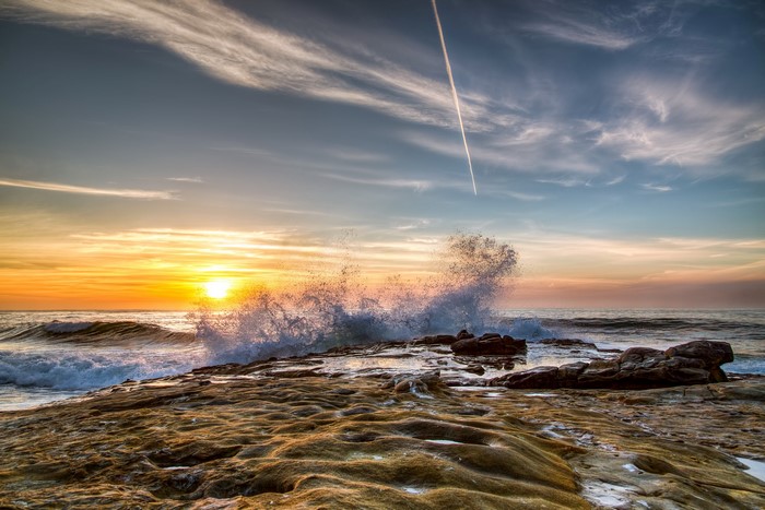 Sunset over the ocean with waves crashing on rocks