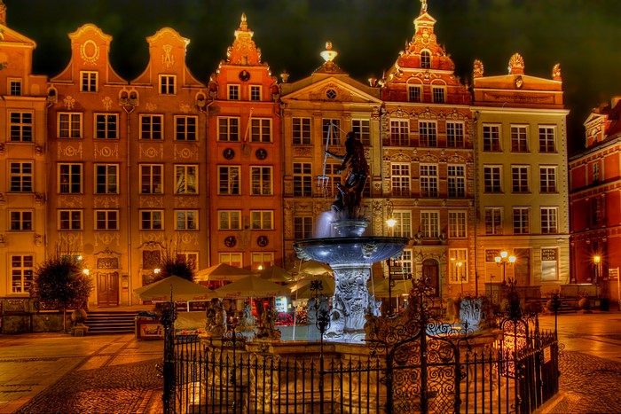 Neptune's Fountain in front of historic buildings at night in Gdansk, Poland