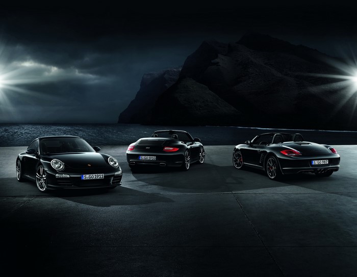 Three black Porsche cars parked by the sea at night