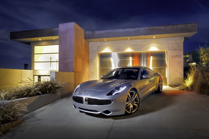 Silver Fisker Karma EVer parked in front of a modern house at night