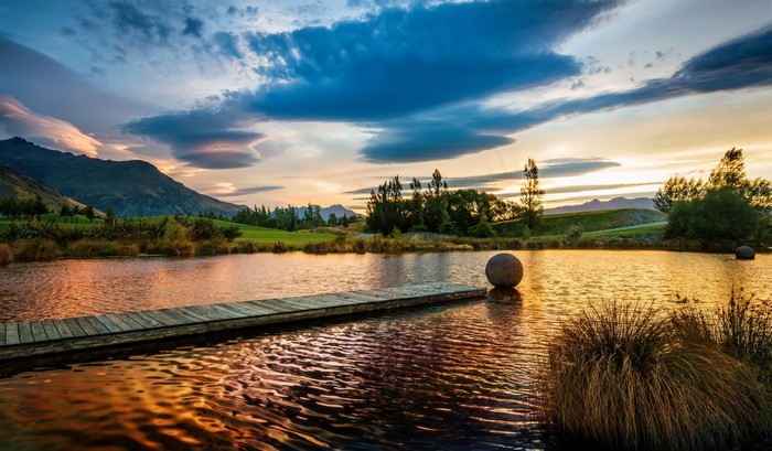 Lake with wooden pier and sphere sculpture at sunset