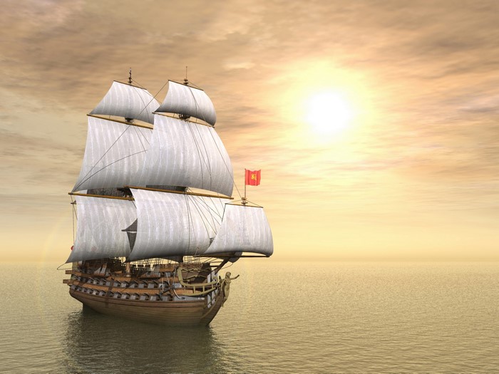 A tall sailing ship with white sails on the sea at sunset