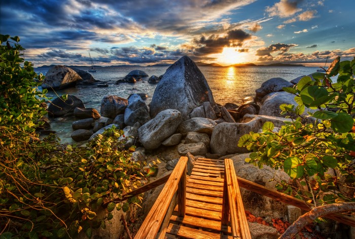 Wooden walkway to the sea with large boulders at sunset