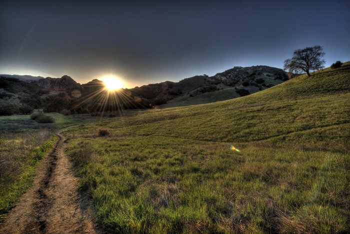 Sunset over a grassy hill with a trail in California