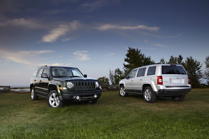 Two Jeep Patriots parked on grass with sky background