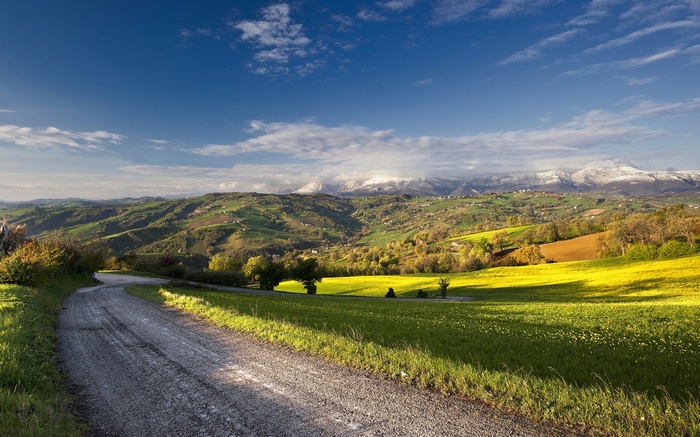 Winding road through rolling hills and snow-capped mountains