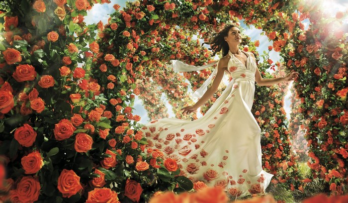 Woman in a rose-adorned dress walking through a rose arch
